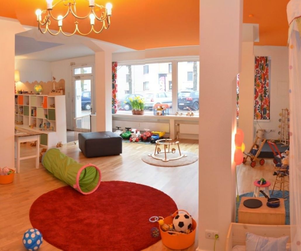 Spielraum mit Klavier, rotem Teppich, Krabbeltunnel und verschiedenen Spielzonen